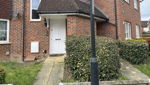 Uma casa de dois andares de tijolo com porta frontal branca, antenas parabólicas e uma pequena área de jardim.