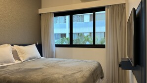 A hotel room with a bed, a window with curtains, and a view of buildings and greenery outside. - TTW - The Town Studios By Anora Spaces (São Paulo)