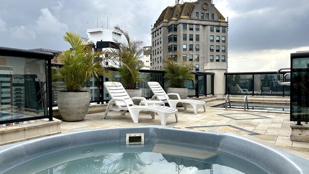 A rooftop pool area with lounge chairs, potted plants, and a view of a tall building in the background. - TTW - The Town Studios By Anora Spaces (São Paulo)