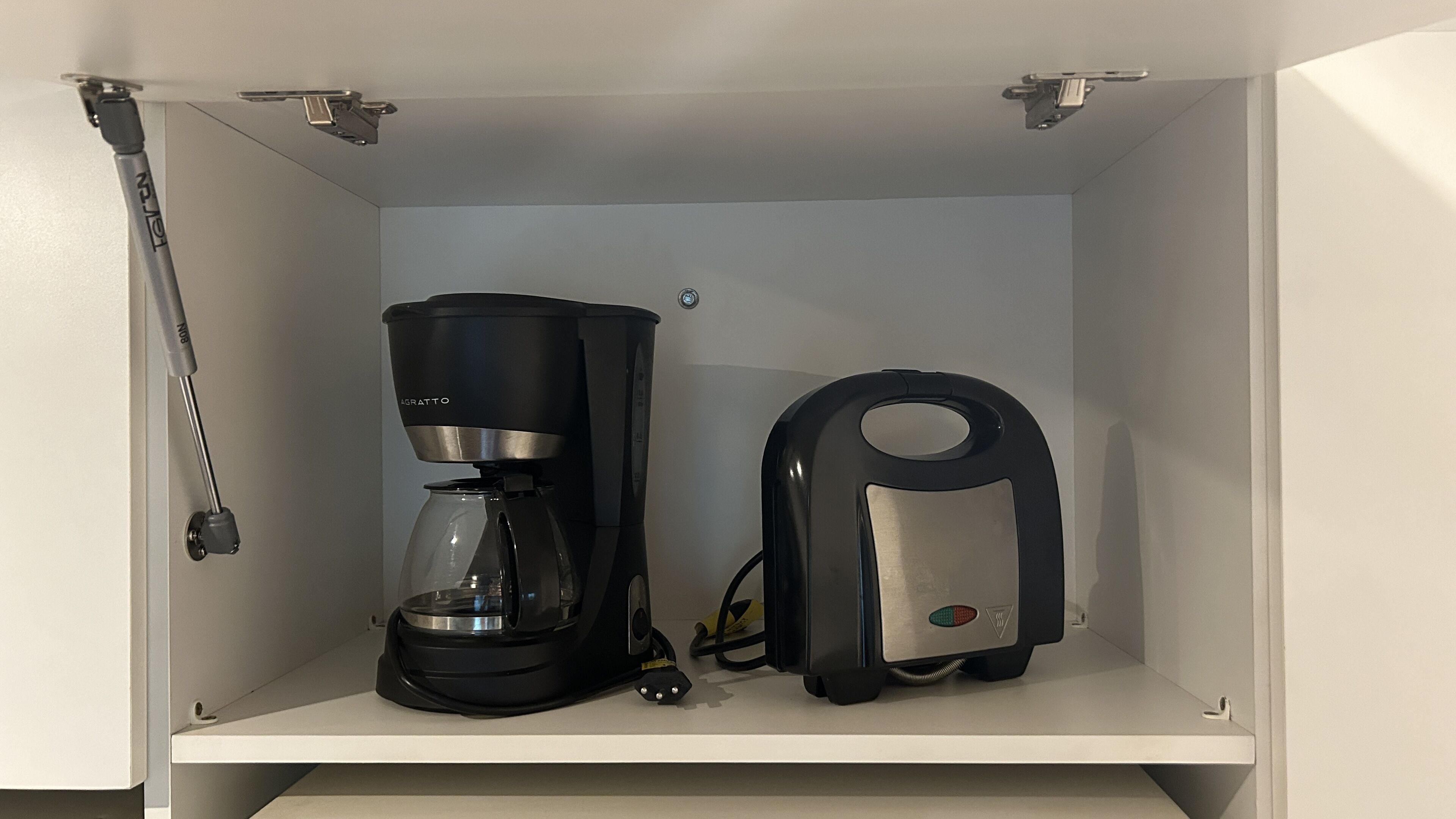 A coffee maker and a kettle in a white cabinet.