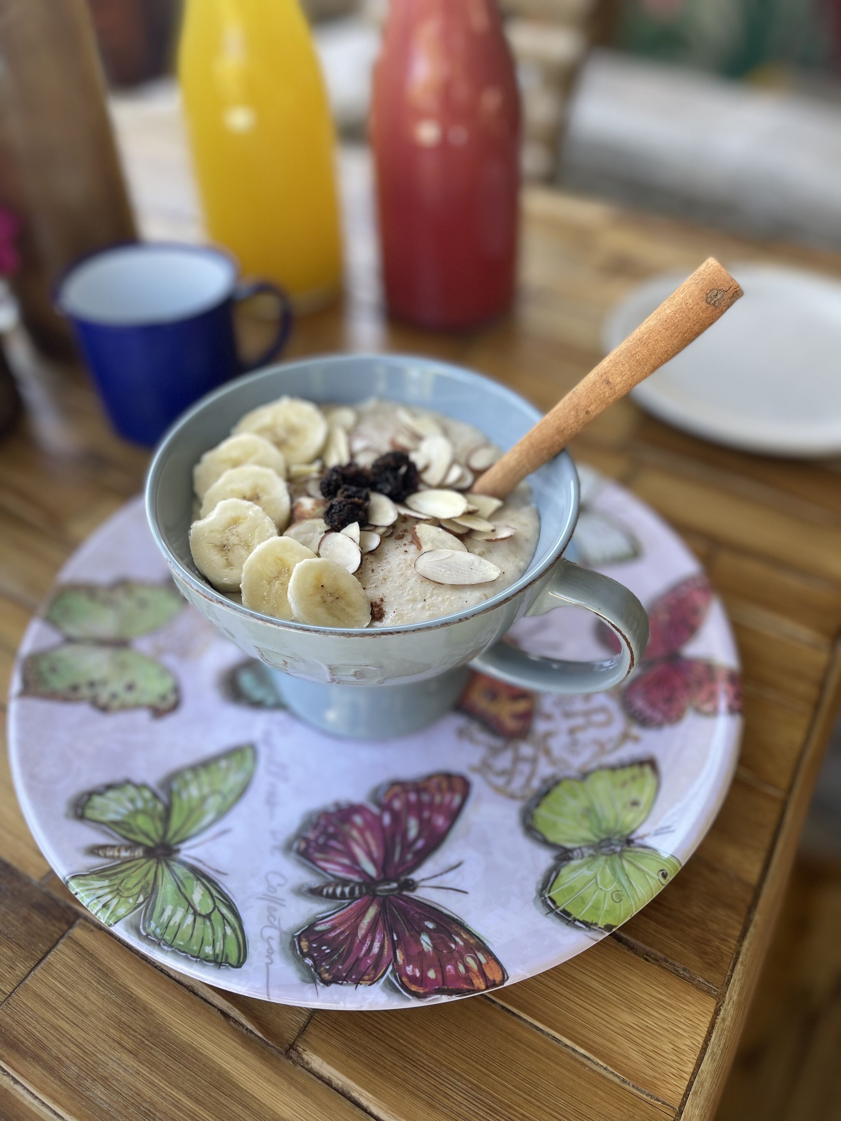 A bowl of oatmeal with banana slices, almonds, and raisins on a plate with butterfly designs.