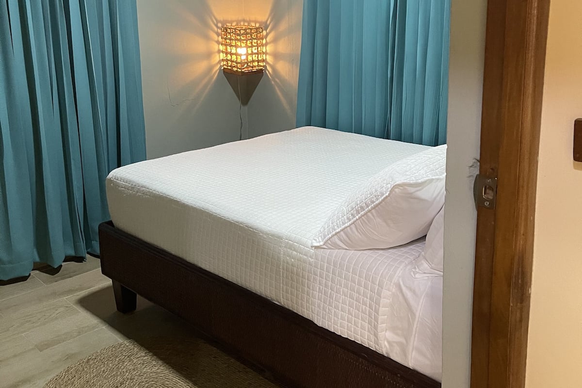 Une chambre à coucher avec un lit, des rideaux, un luminaire fixé au mur et un plafond en bois.