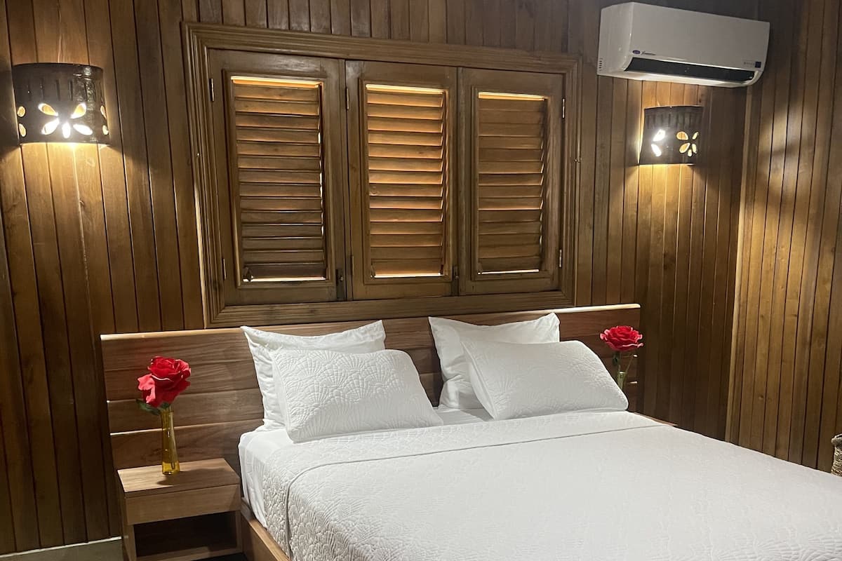 Une chambre à coucher avec une tête de lit en bois, un couvre-lit blanc et deux tables de chevet avec des lampes.