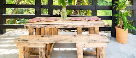A rustic wooden picnic table with benches, surrounded by a black wooden fence and lush greenery.