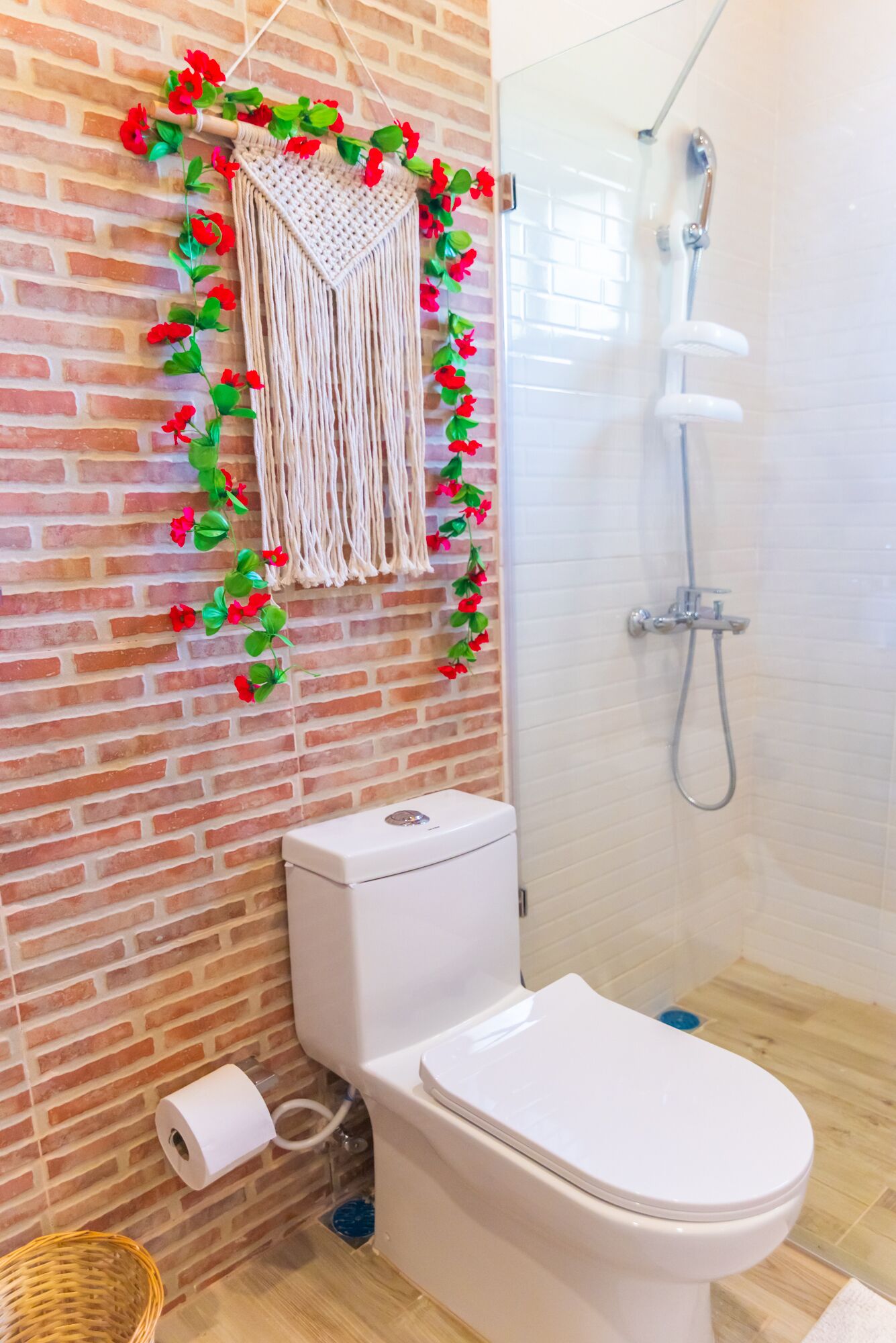 Un baño con inodoro, ducha y un colgador decorativo de macramé con flores rojas.