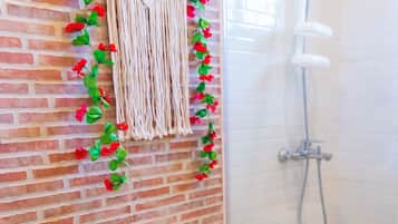 Un baño con inodoro, ducha y un colgador decorativo de macramé con flores rojas.