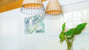 Un comedor de madera con una mesa dispuesta para dos personas, dos lámparas colgantes tejidas, una planta verde y un florero con flores.