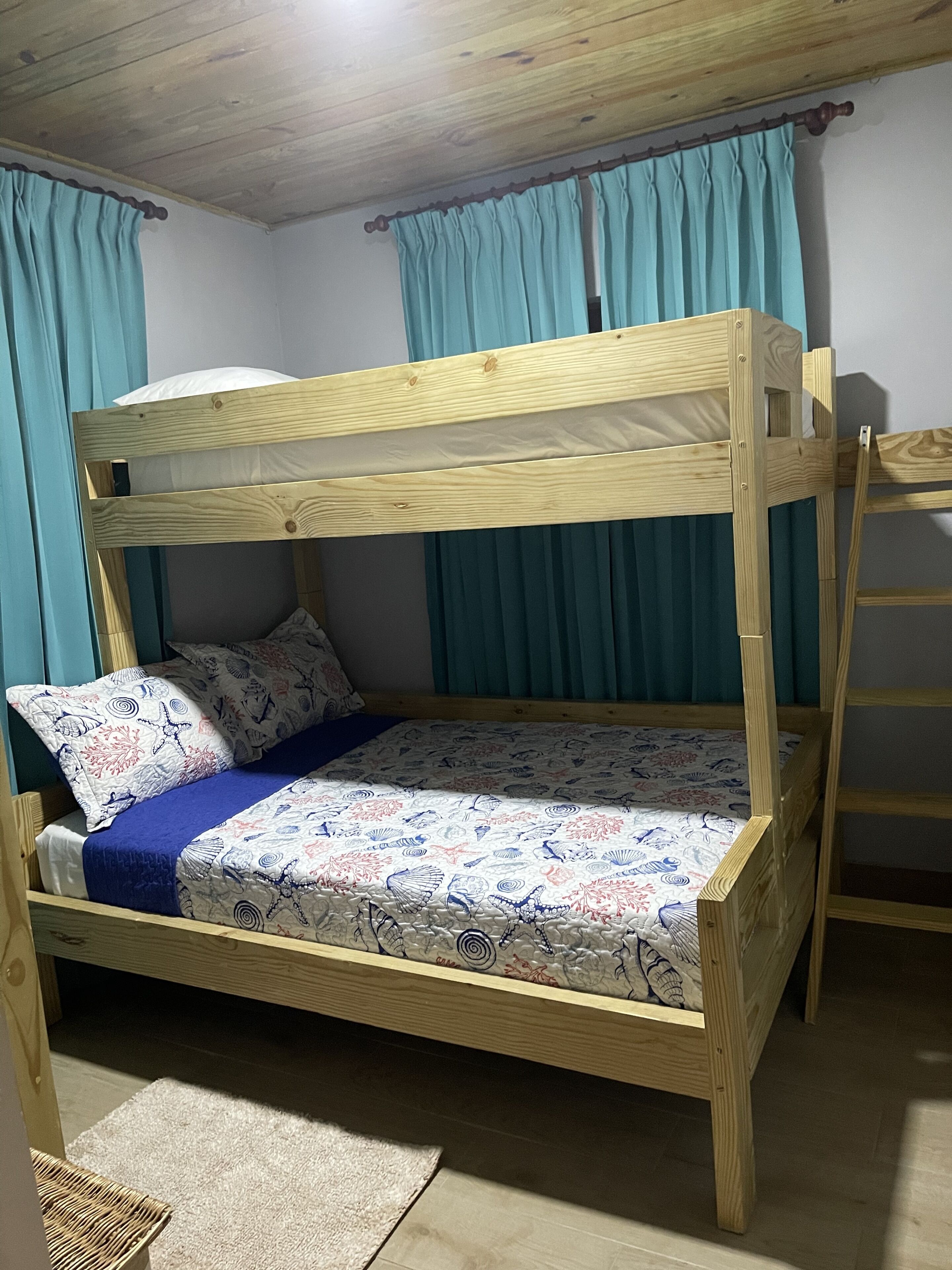 Ein Holzbett mit Etagen, einer gemusterten Bettdecke, zwei Kissen und einer blauen Decke.