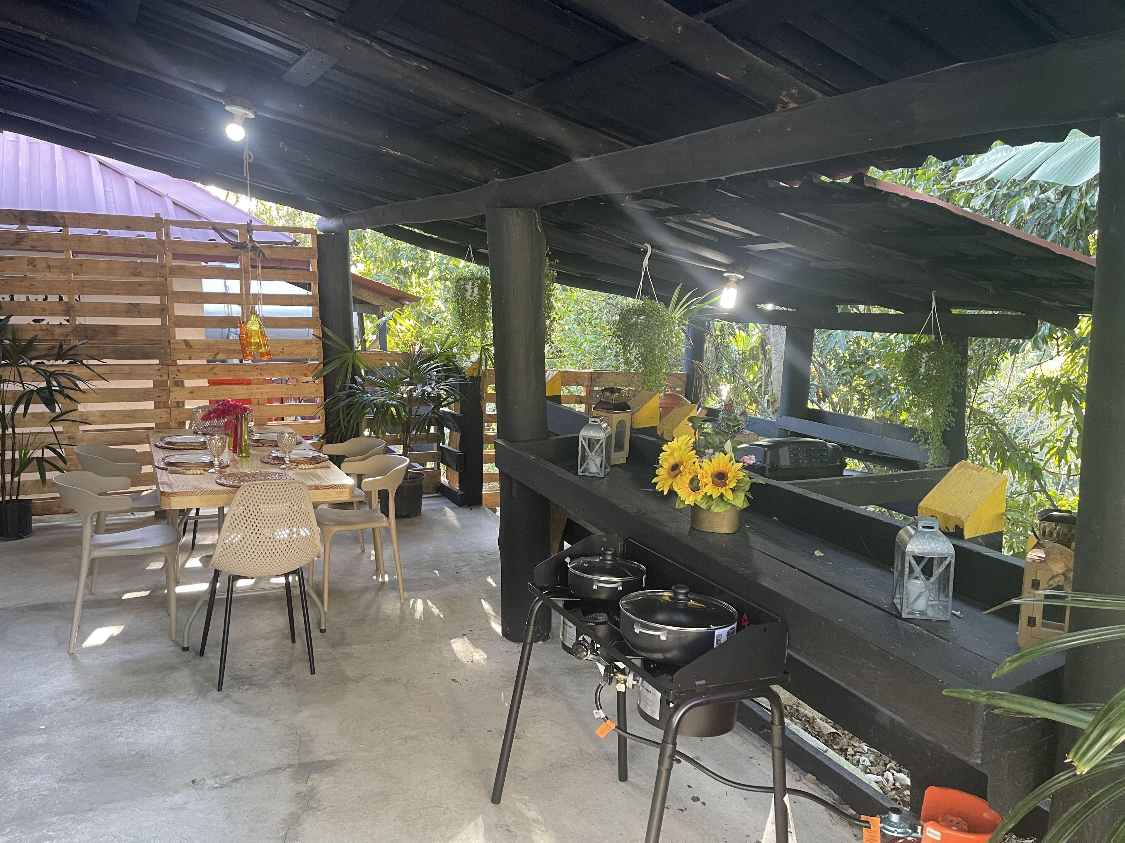 Een buitenterras met houten tafels en stoelen, een grillplaats en potplanten.