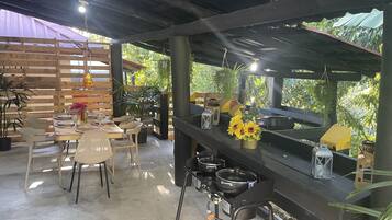 Een buitenterras met houten tafels en stoelen, een grillplaats en potplanten.