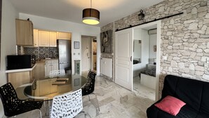 A modern kitchen with a dining area, a black couch with a pink pillow, and a stone wall. - Bright 31m2, flowered terrace, near Croisette (Cannes)