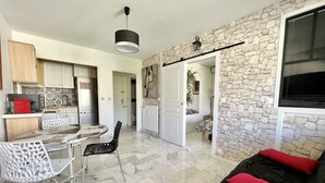 A modern kitchen with white cabinets, a dining area with a glass table, and a living area with a stone wall and a black sofa. - Bright 31m2, flowered terrace, near Croisette (Cannes)