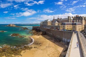 A coastal town with a prominent castle-like building, a sandy beach, and a clear blue sky.