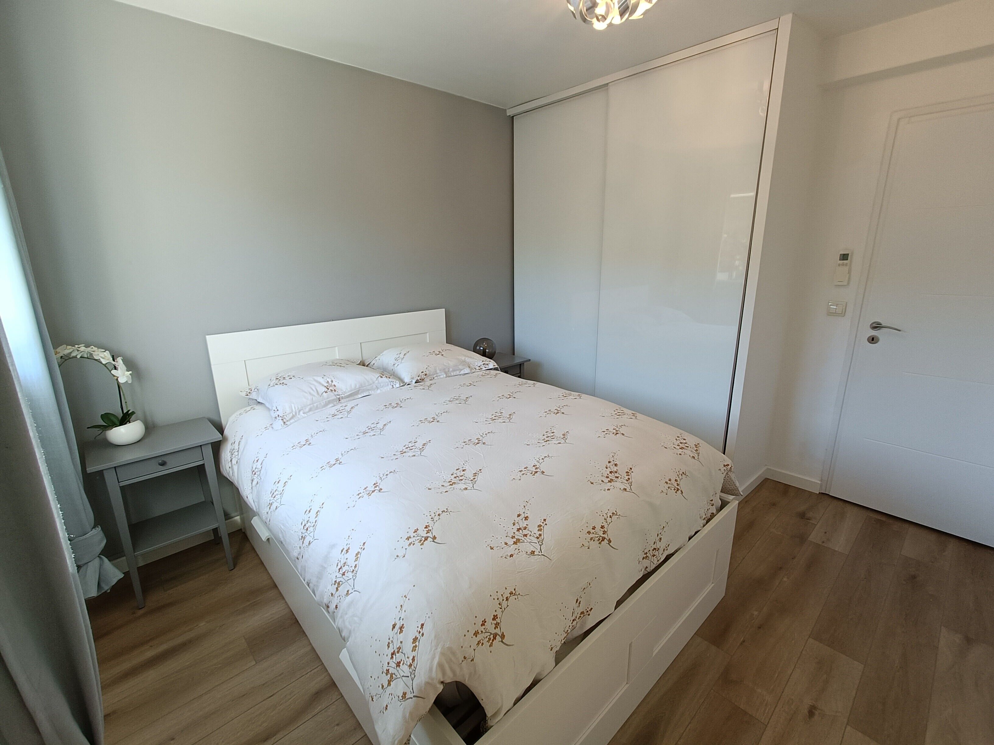 A bedroom with a bed, nightstand, and a potted plant.