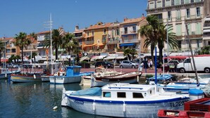 A marina with several boats docked, surrounded by buildings with balconies and palm trees.