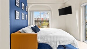 A bedroom with a bed, a TV mounted on the wall, and a balcony with a view of the outside. - Emerald City Pentouse (Seattle)
