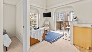 A spacious room with a large bed, a desk, and a chair. There is a TV mounted on the wall and a window providing a view of the city. - Emerald City Pentouse (Seattle)