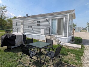 A mobile home with a patio area featuring a table and chairs, a grill, and a covered outdoor seating area.