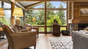Una sala de estar acogedora con chimenea, ventanas amplias y vistas a árboles.