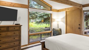 Un dormitorio con un ventanal grande, vigas de madera, una cama, un aparador y un televisor.