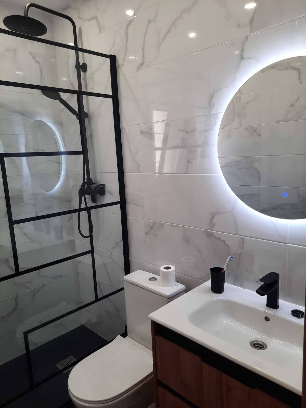 Et moderne badeværelse med en glasbrusekabine, toilet, vask med spejl og marmorfliser.
