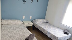 Una habitación con dos camas, una mesita blanca y una pared decorada.