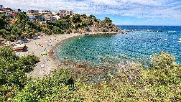 Una playa costera con aguas cristalinas, una orilla arenosa y edificios en una ladera.
