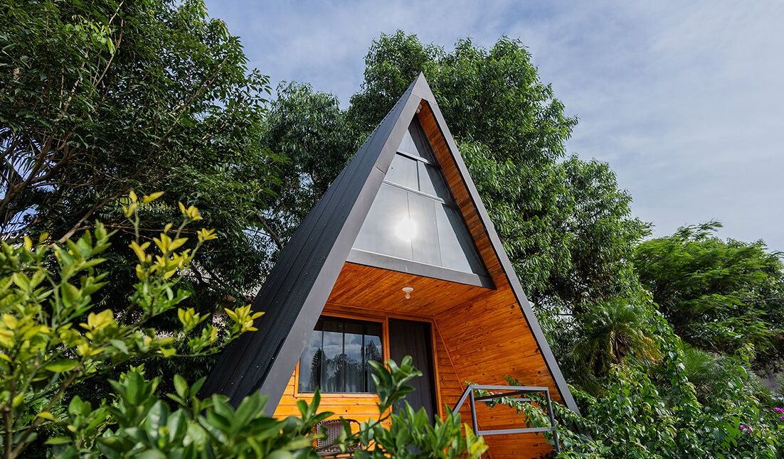 A modern, triangular-shaped cabin surrounded by lush greenery.