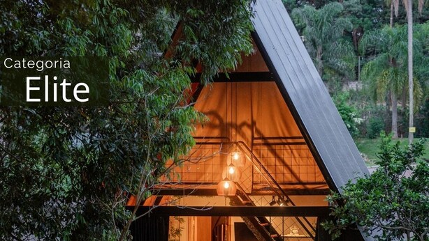An 'Elite' category building with a wooden exterior, a visible staircase, and a dining area with chairs and tables. - Recanto Catarina (Cascavel)