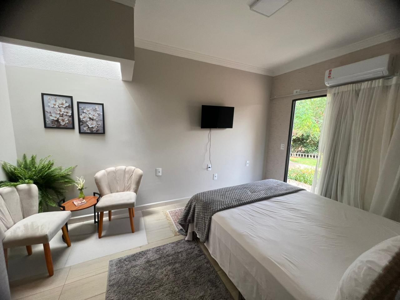 A bedroom with a bed, two armchairs, a small table, a TV, and a window with curtains.