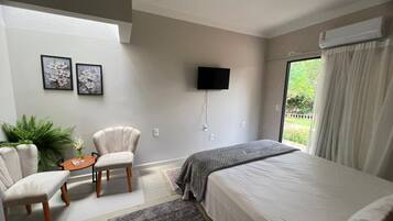 A bedroom with a bed, two armchairs, a small table, a TV, and a window with curtains.
