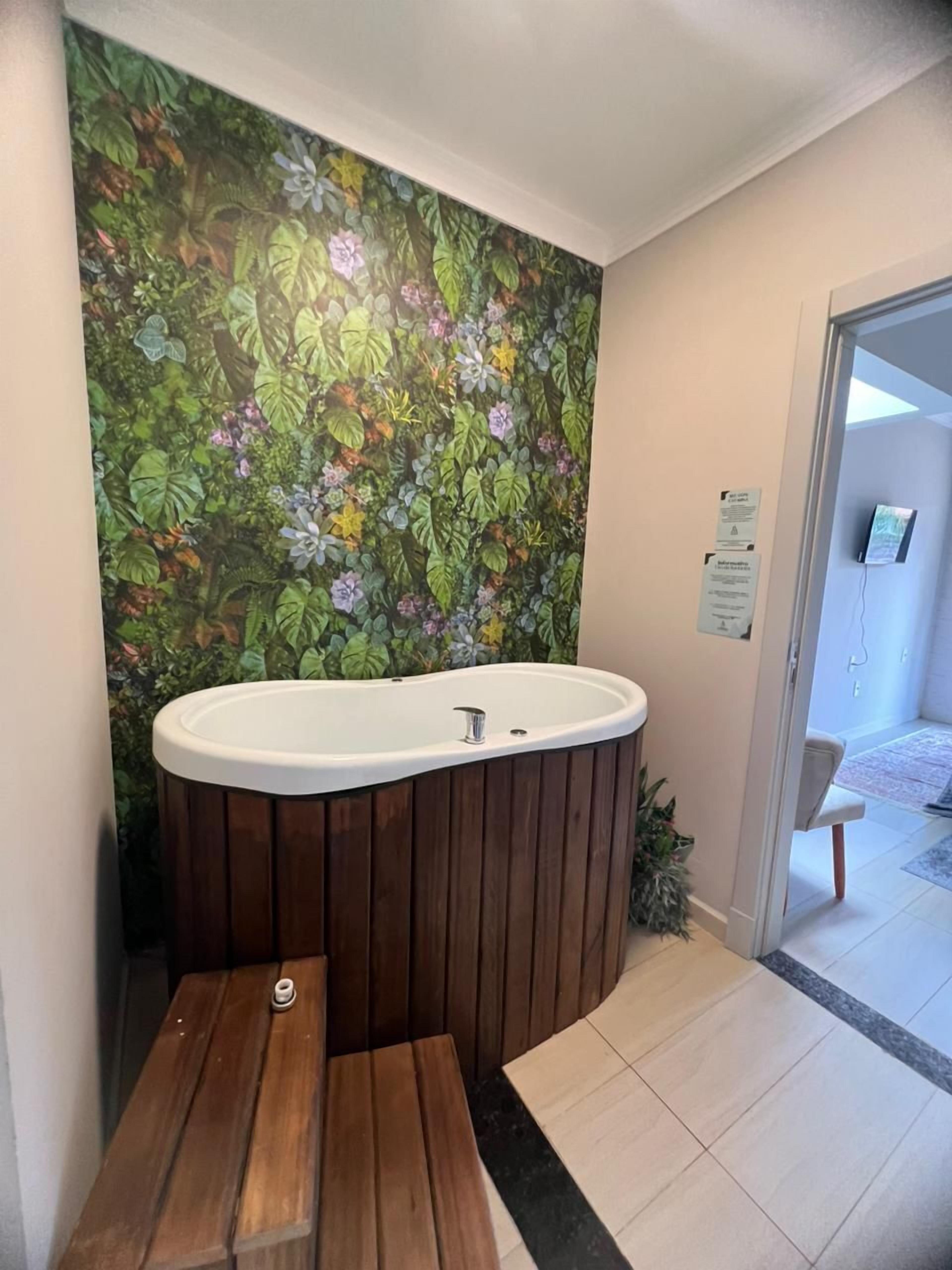 A bathroom with a wooden bench, a freestanding bathtub, and a floral mural on the wall.