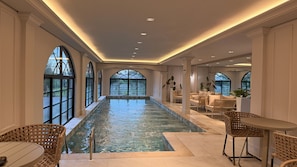 Una amplia piscina interior con zonas de estar y grandes ventanales.