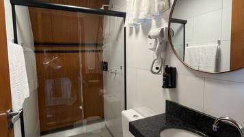 Un baño moderno con ducha envuelta en vidrio, inodoro blanco, lavamanos de mármol negro y un espejo grande.