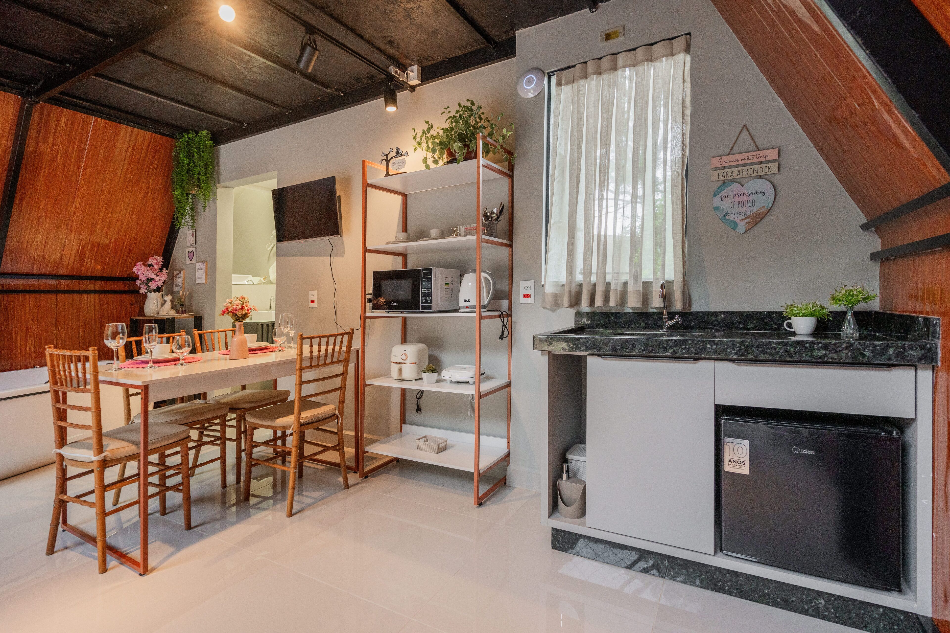 Uma cozinha compacta com área de refeições, cadeiras de madeira, uma mesa branca, uma geladeira preta e um micro-ondas.