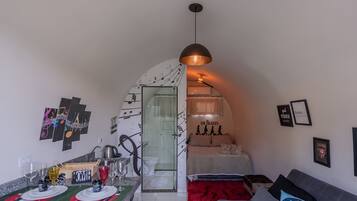 A compact living space with a kitchenette, a dining area, a bedroom with a red rug, and a wall with musical notes and a Beatles poster.