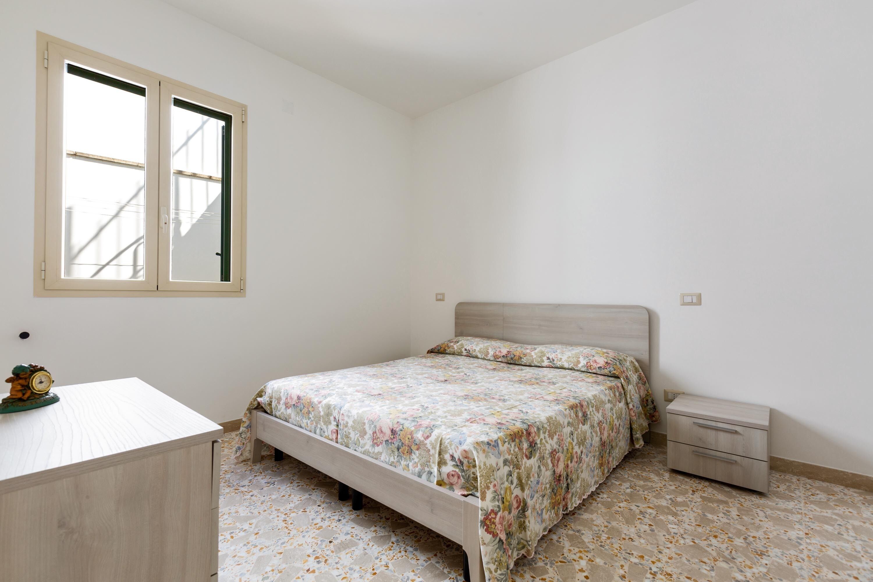 Une chambre à coucher avec un lit, une table de chevet, une commode et une fenêtre.