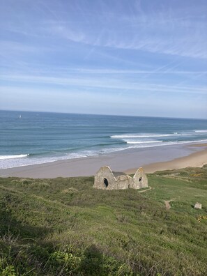 A coastal landscape with a beach, waves, and a ruined structure. - Sympathique Maison Proche de la mer au Calme (Barneville-Carteret)