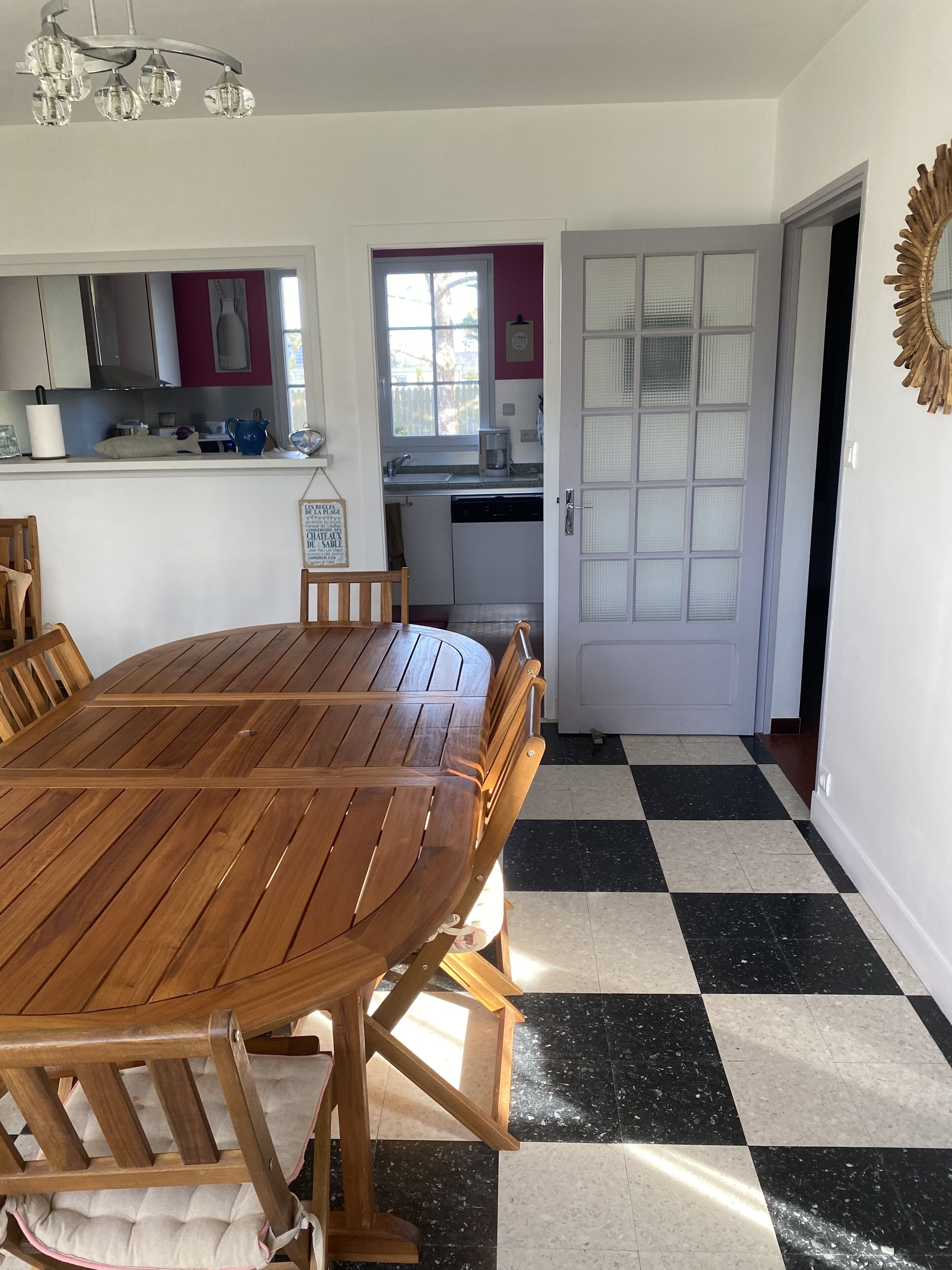 A dining area with a wooden table and chairs, a kitchen with white cabinets and a window, and a checkered floor.