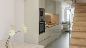 Une cuisine moderne dotée d’appareils électroménagers intégrés, d’un escalier en bois et donnant sur l’espace de vie adjacent.