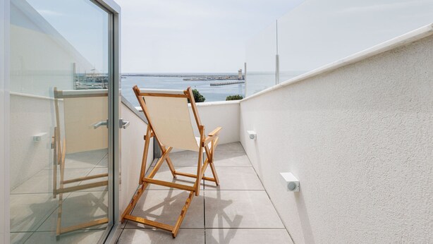 Un balcon avec vue sur la mer, une chaise en bois et une porte vitrée.