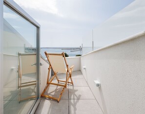 En balkon med havudsigt, en træstol og en glasdør.