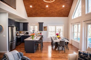A spacious kitchen with dark cabinets, a central island, and a dining area with a table and chairs. - Modern Luxury Rustic Home at Lake | Dogs Welcome (Farmington)