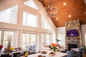 A spacious room with large windows, a stone fireplace, and a chandelier. - Modern Luxury Rustic Home at Lake | Dogs Welcome (Farmington)