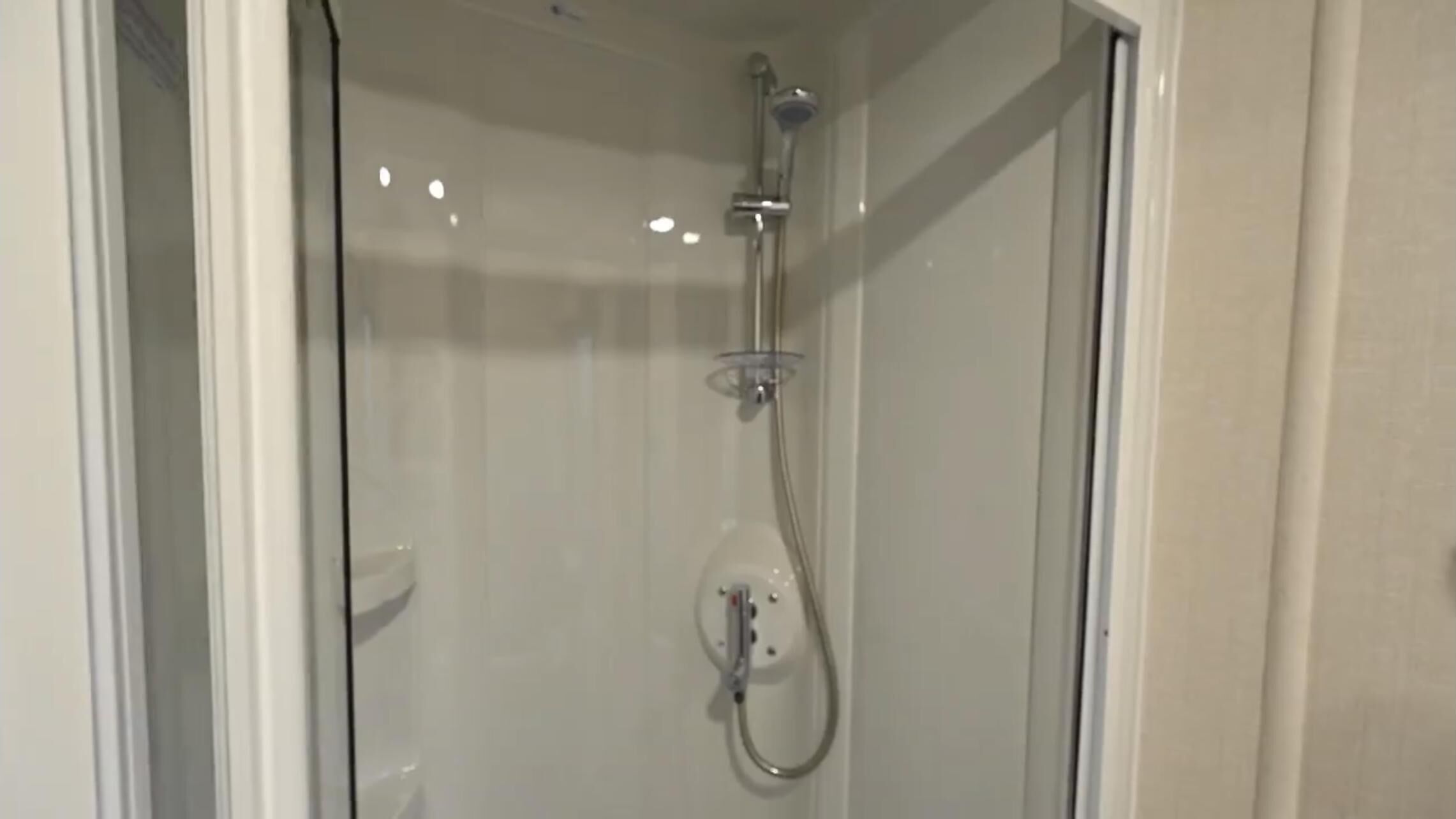 A glass-enclosed shower with a handheld showerhead and a wall-mounted faucet.