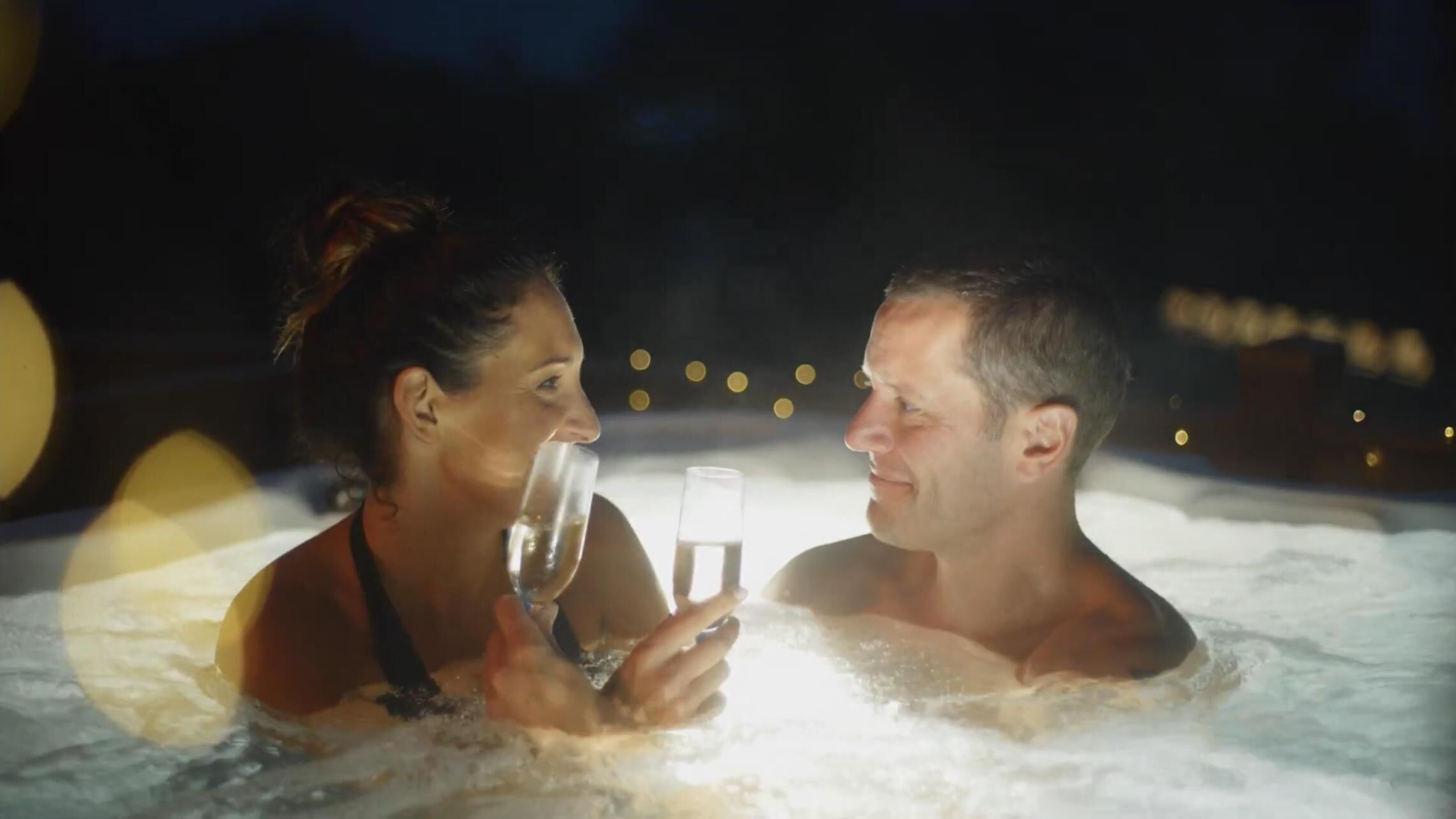Dos personas en un jacuzzi por la noche.