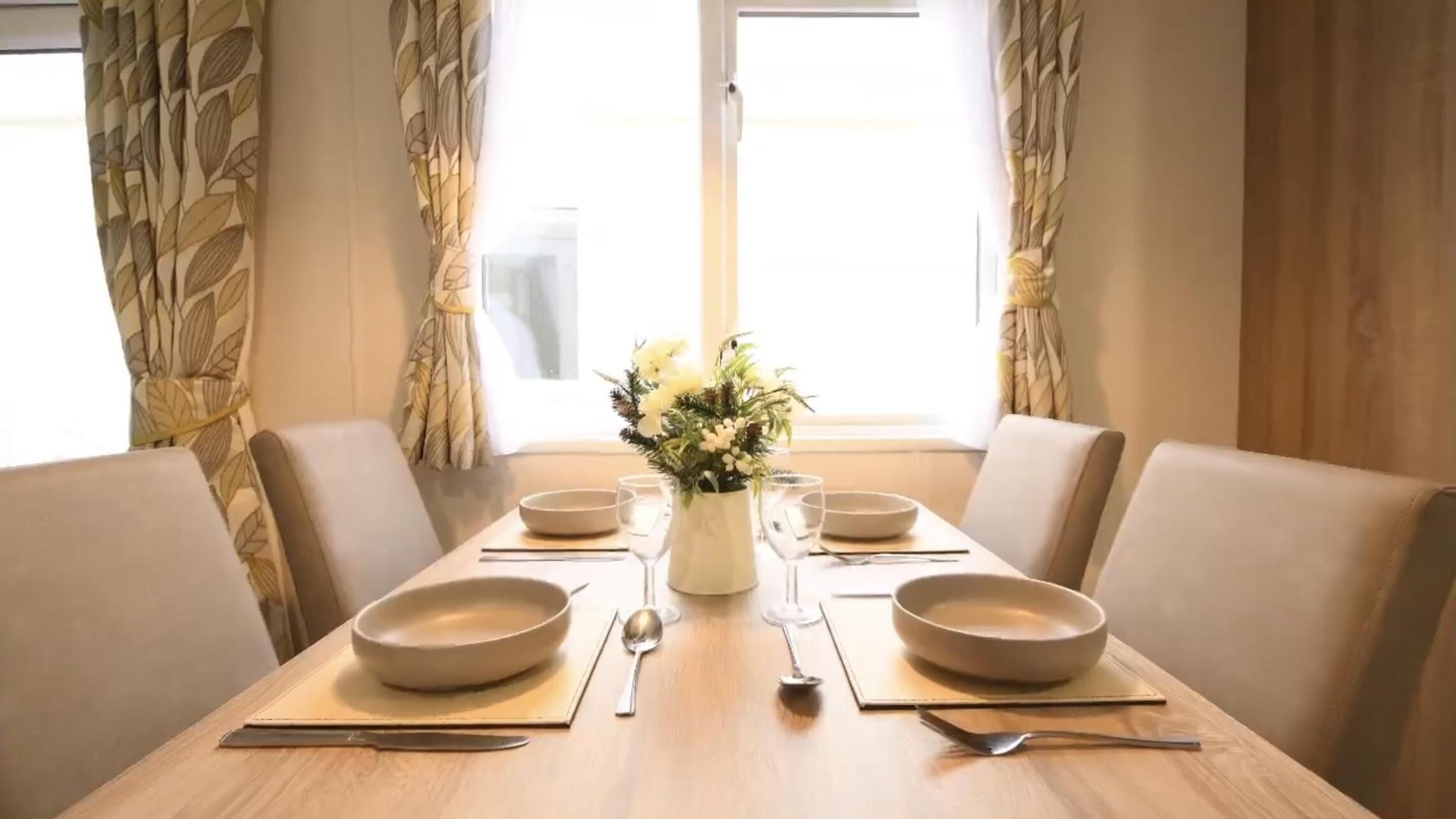 A dining table set for four with a vase of flowers, two bowls, and cutlery.