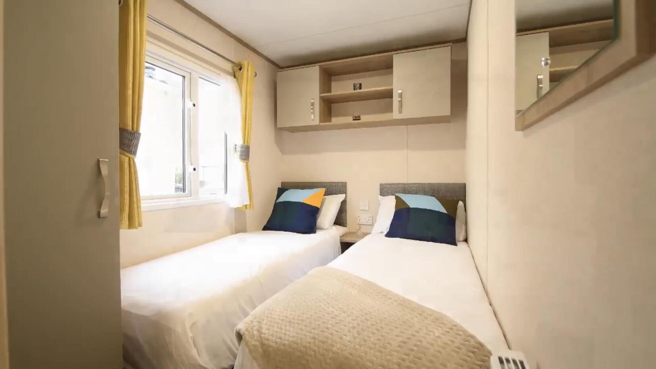 A compact hotel room with two single beds, a small bedside table, a wardrobe, and a window with curtains.