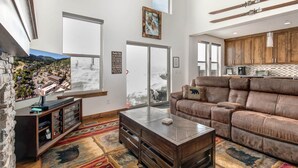 A spacious living room with a large brown leather sofa, a wooden coffee table, and a stone fireplace.
