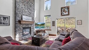 A living room with a stone fireplace, a television, a couch, and a large window with a view of a mountain landscape.